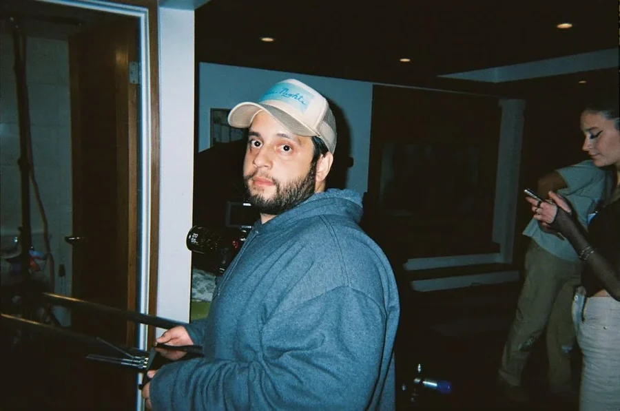 Marcos Segura in a cap and blue hoodie holding a camera rig on set